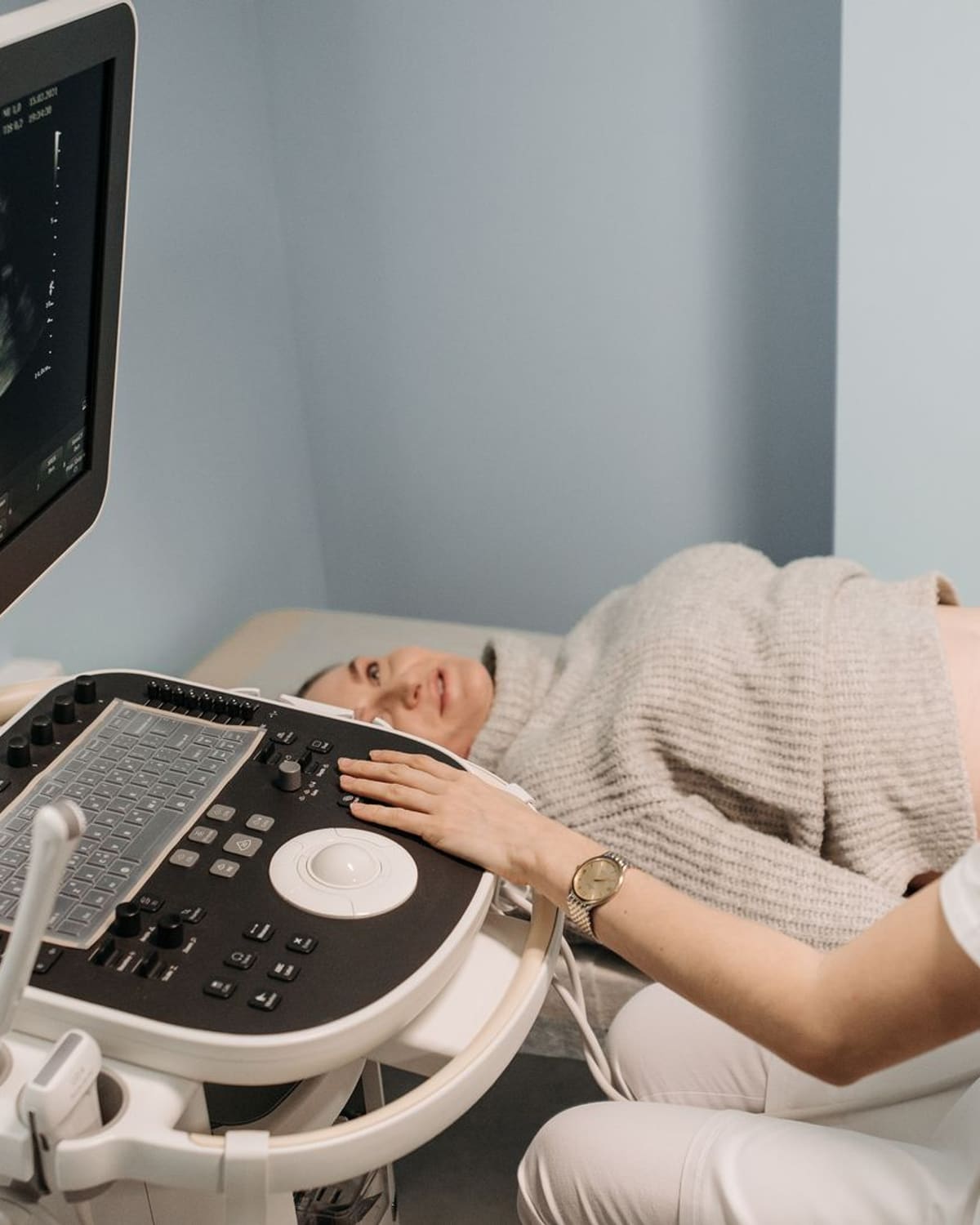 A sonographer moves the probe across a patient's belly, watching the image resolve on screen.