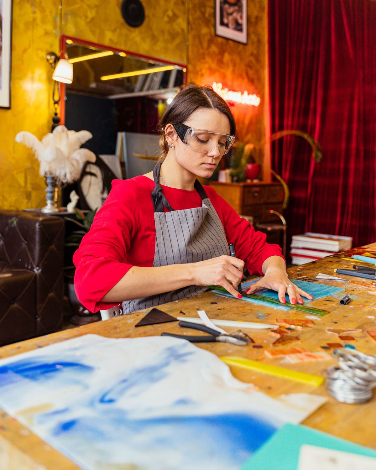 A stained-glass artist scoring a piece of colored glass at the bench