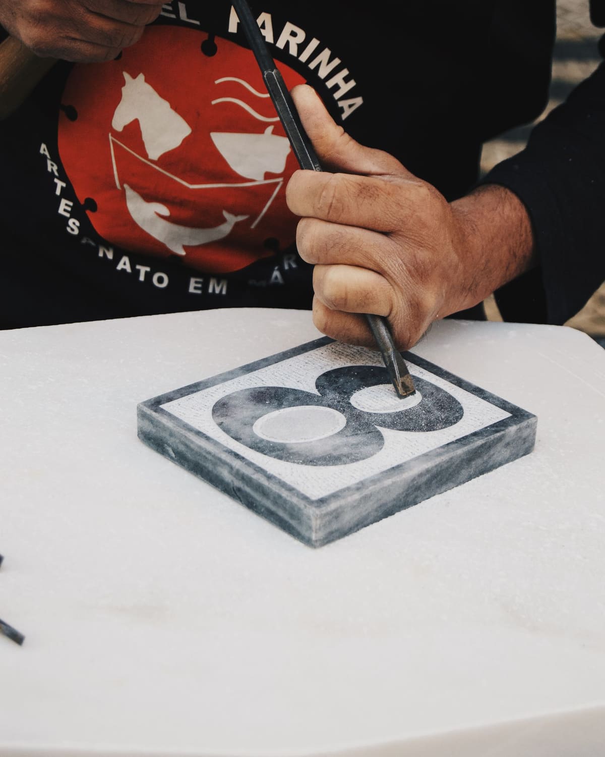 A stonemason's hands carving a numeral into marble with a chisel