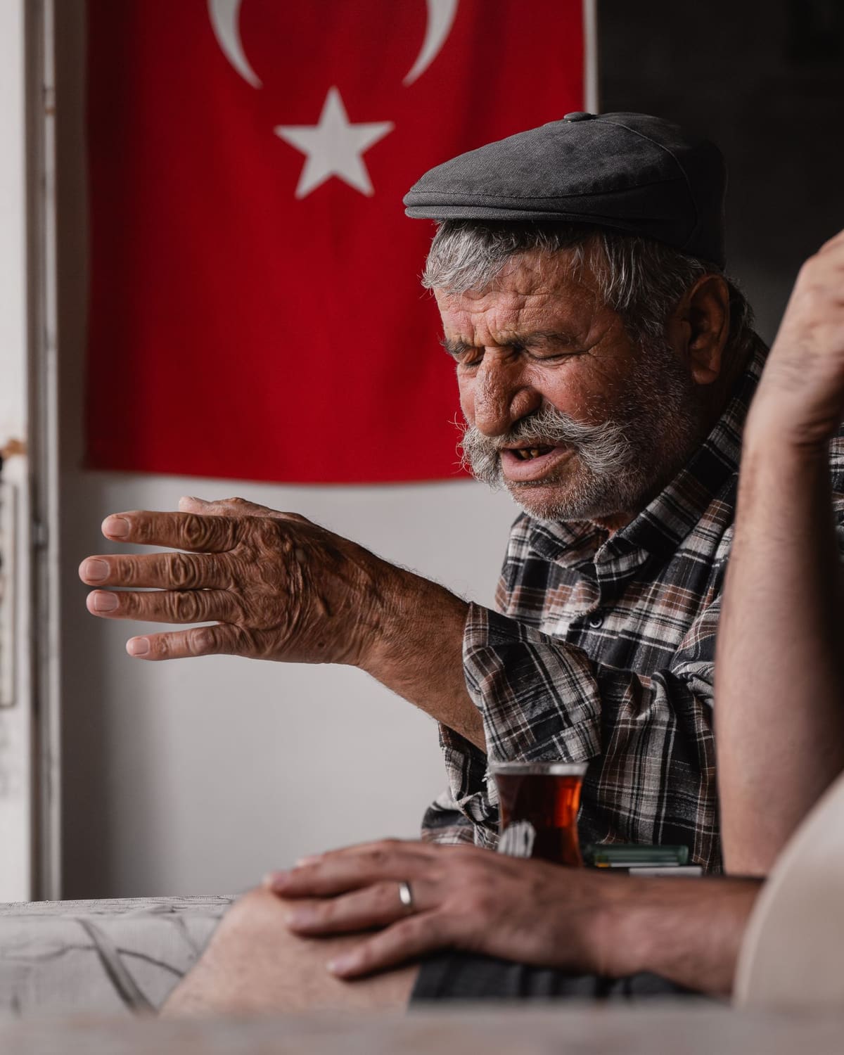 An animated elder telling a story with his hands over a glass of tea