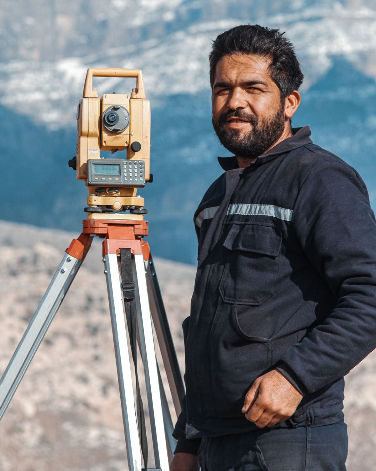 A land surveyor beside a total station in a mountain landscape