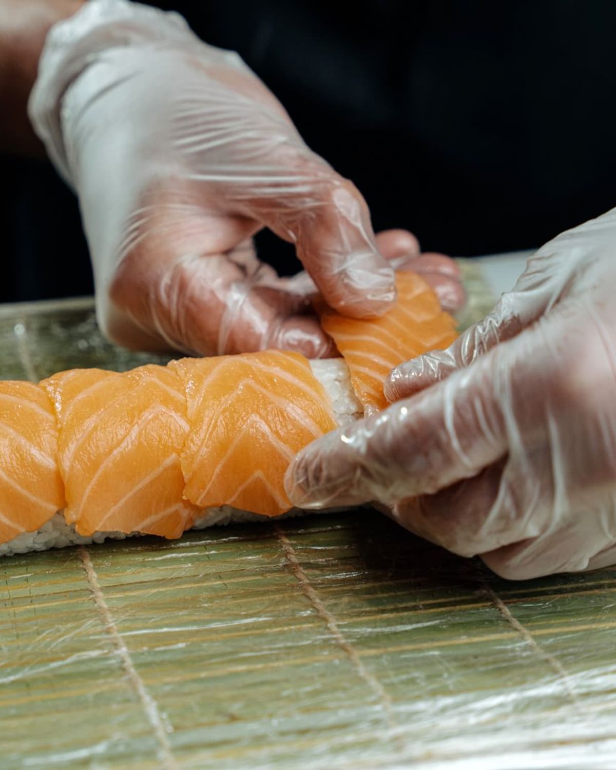 A sushi chef's hands pressing salmon over rice on a bamboo mat