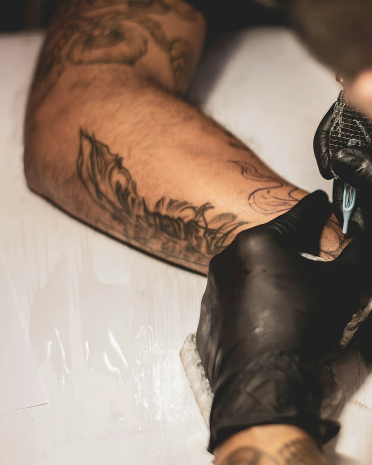 A tattoo artist's gloved hands working a machine on a client's arm