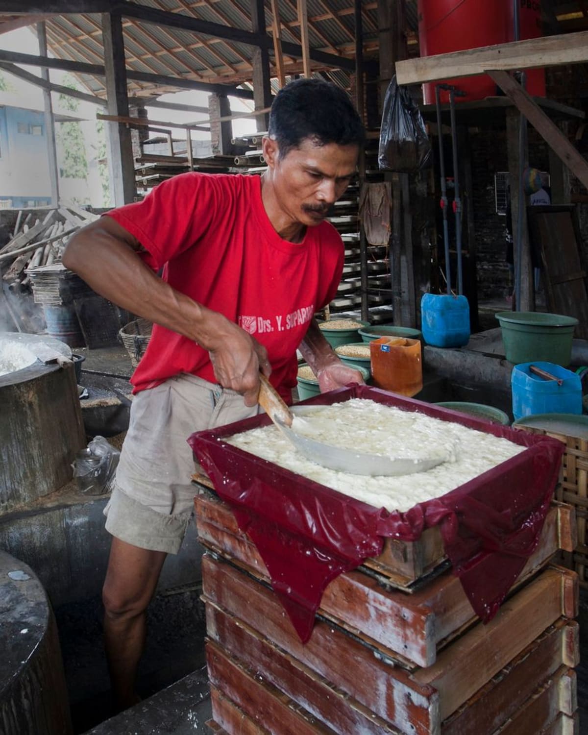 A tofu maker pressing fresh soybean curd into a mold in a workshop.