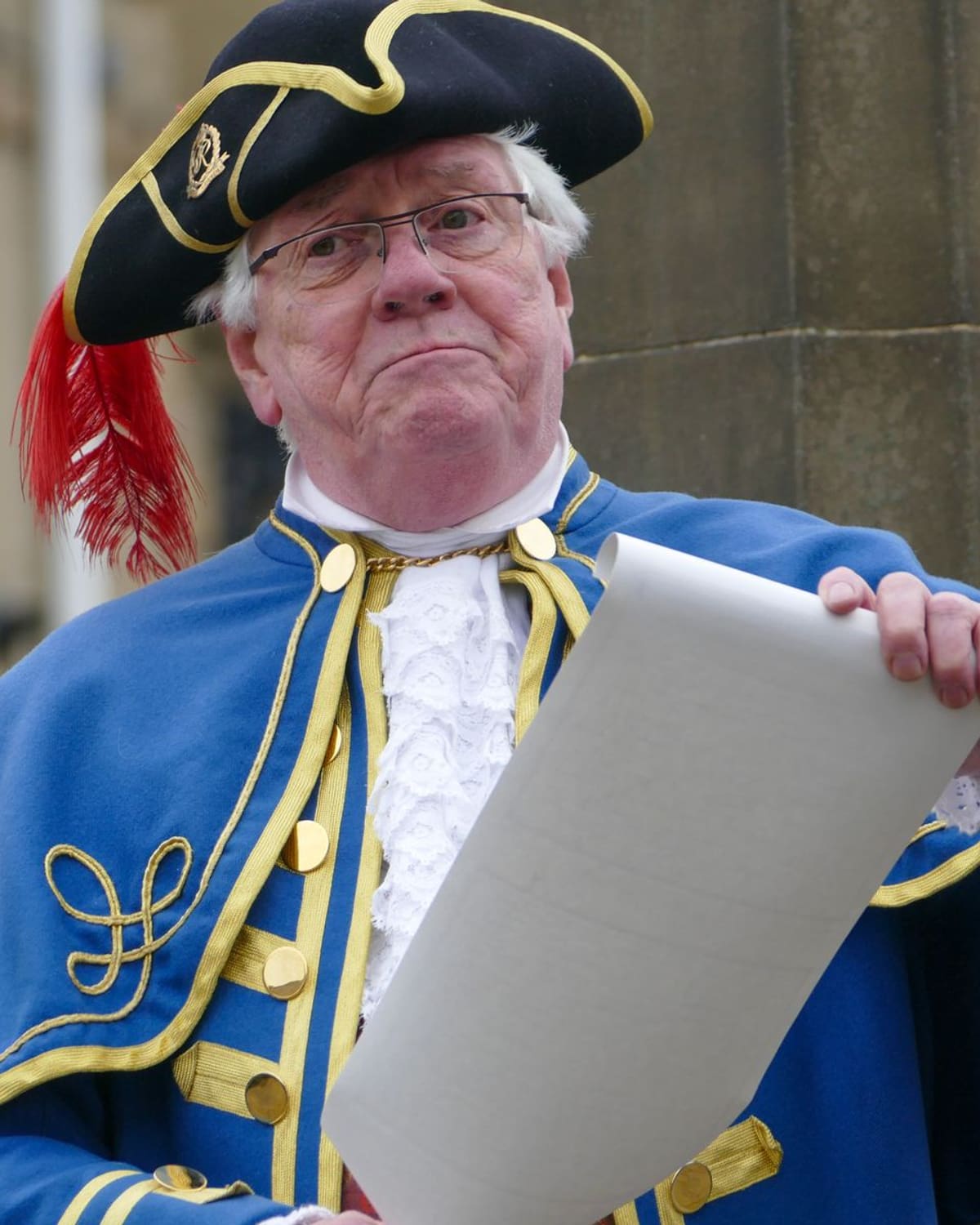 A town crier in traditional costume reading a proclamation from a scroll