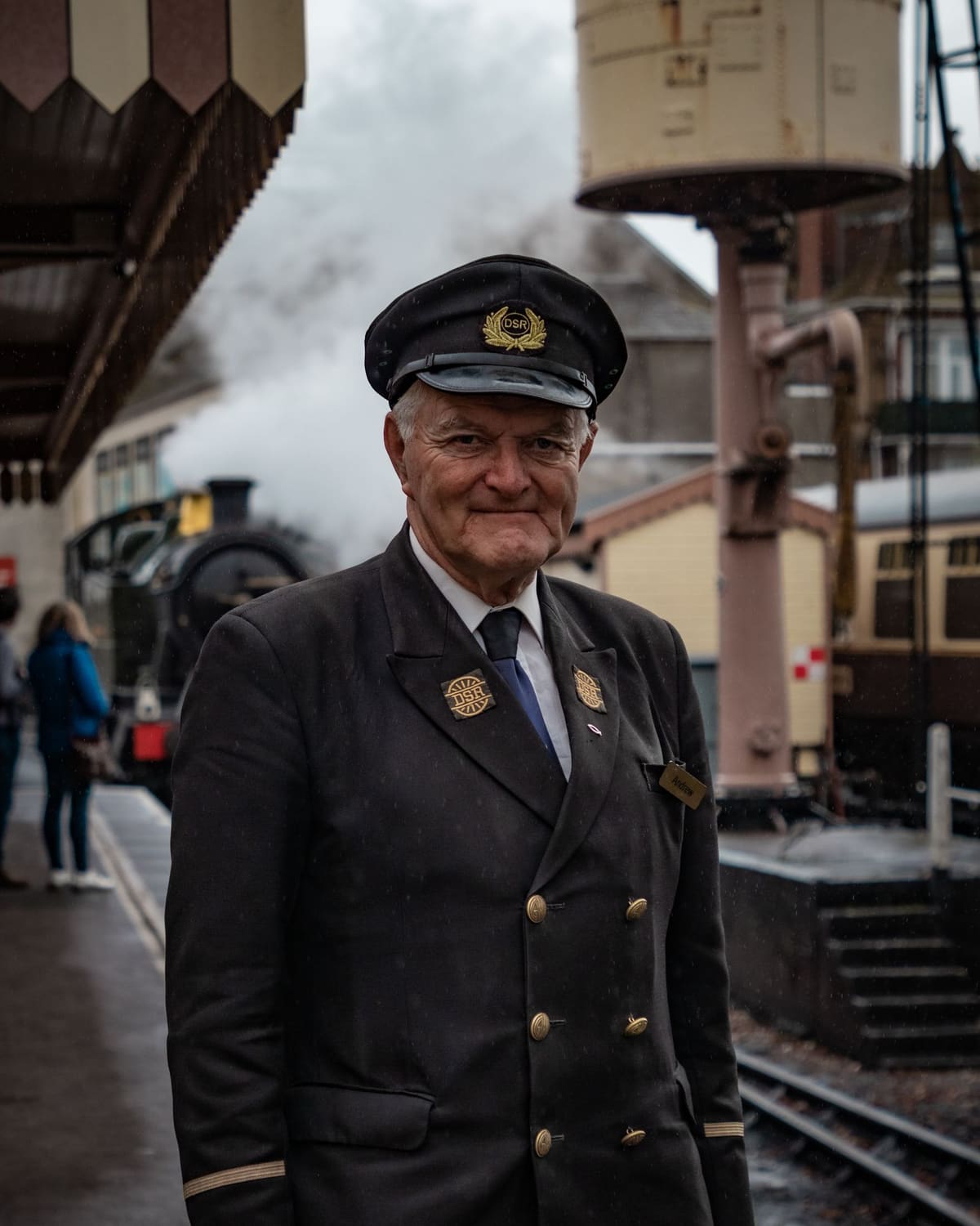 An elderly train conductor in uniform on a steam-railway platform