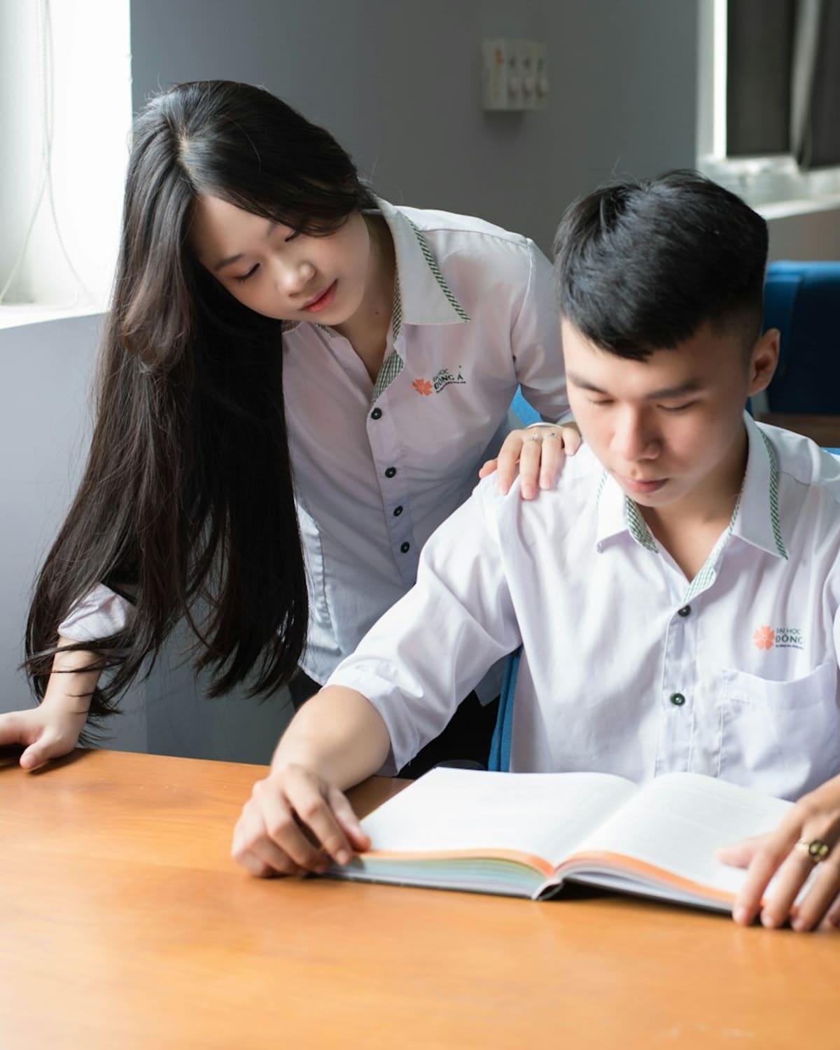 A tutor leaning over a student's open book, pointing at the page