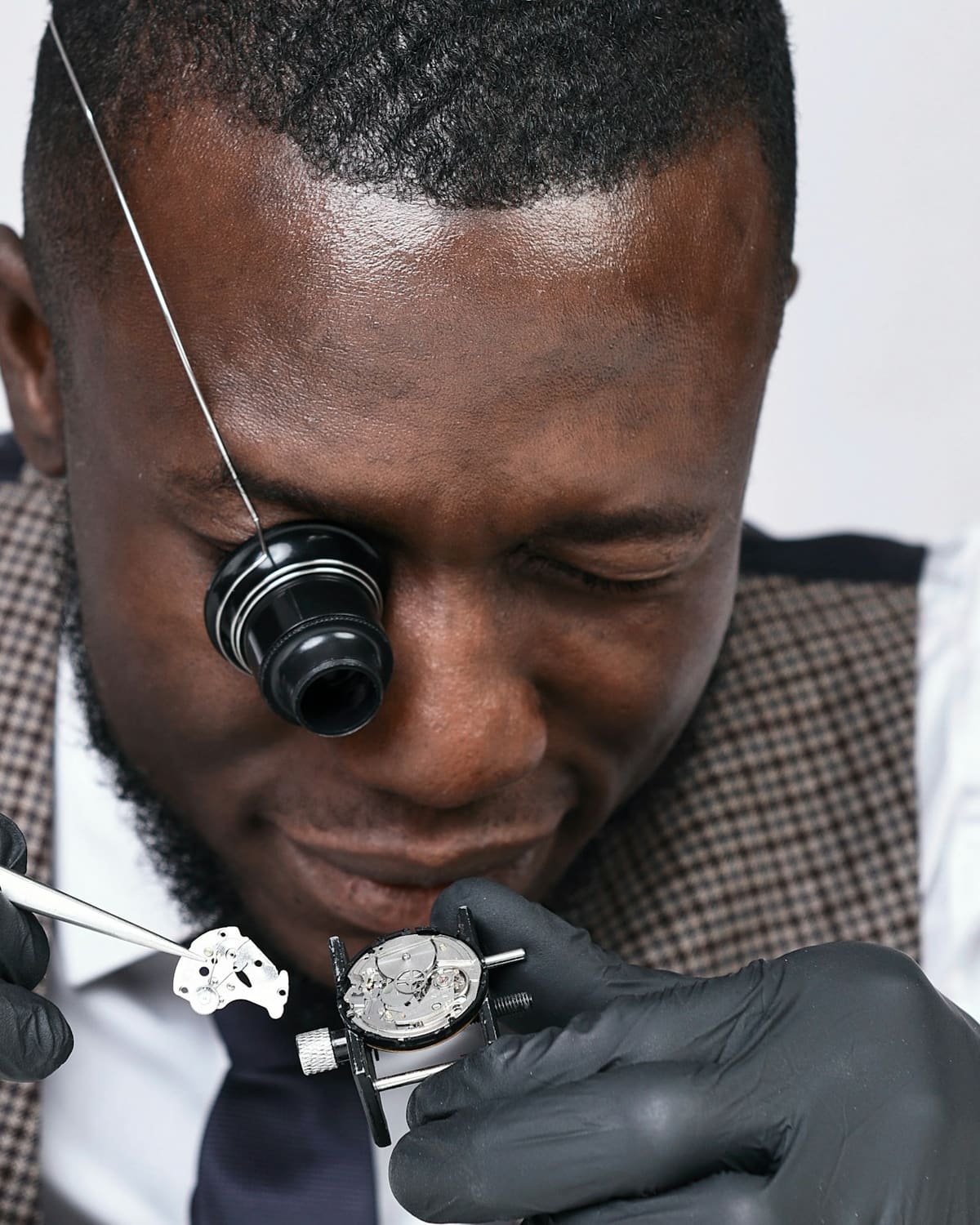 A watchmaker with a loupe, tweezers lifting a tiny watch part