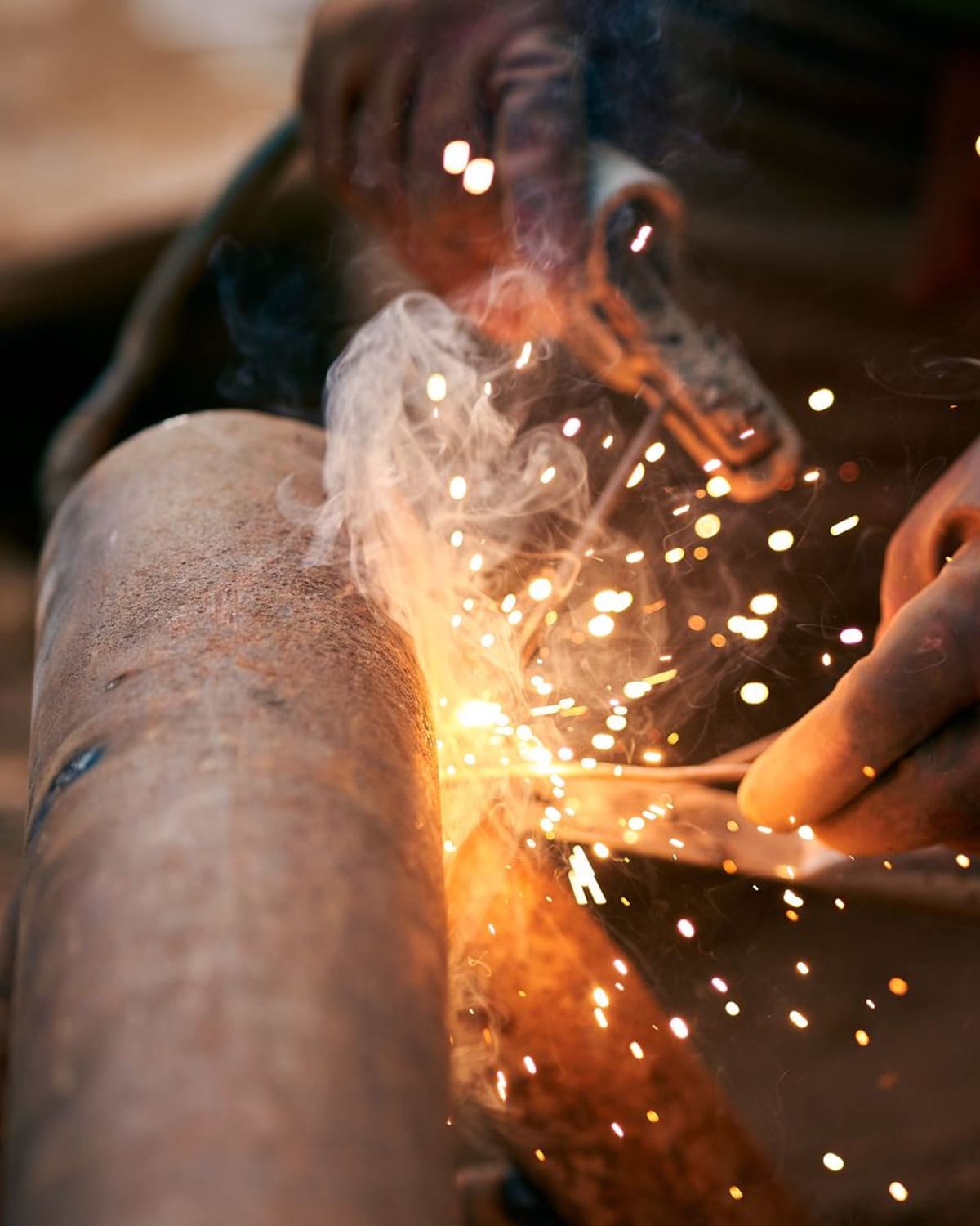 Close-up of a welder's hands joining metal, bright sparks and smoke rising in warm golden light.