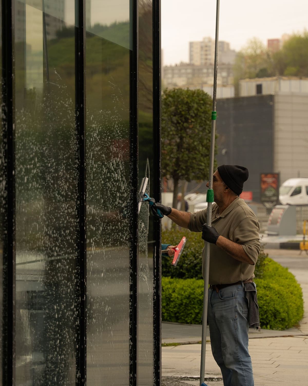 A window cleaner drawing a squeegee down a large glass facade on a city street.
