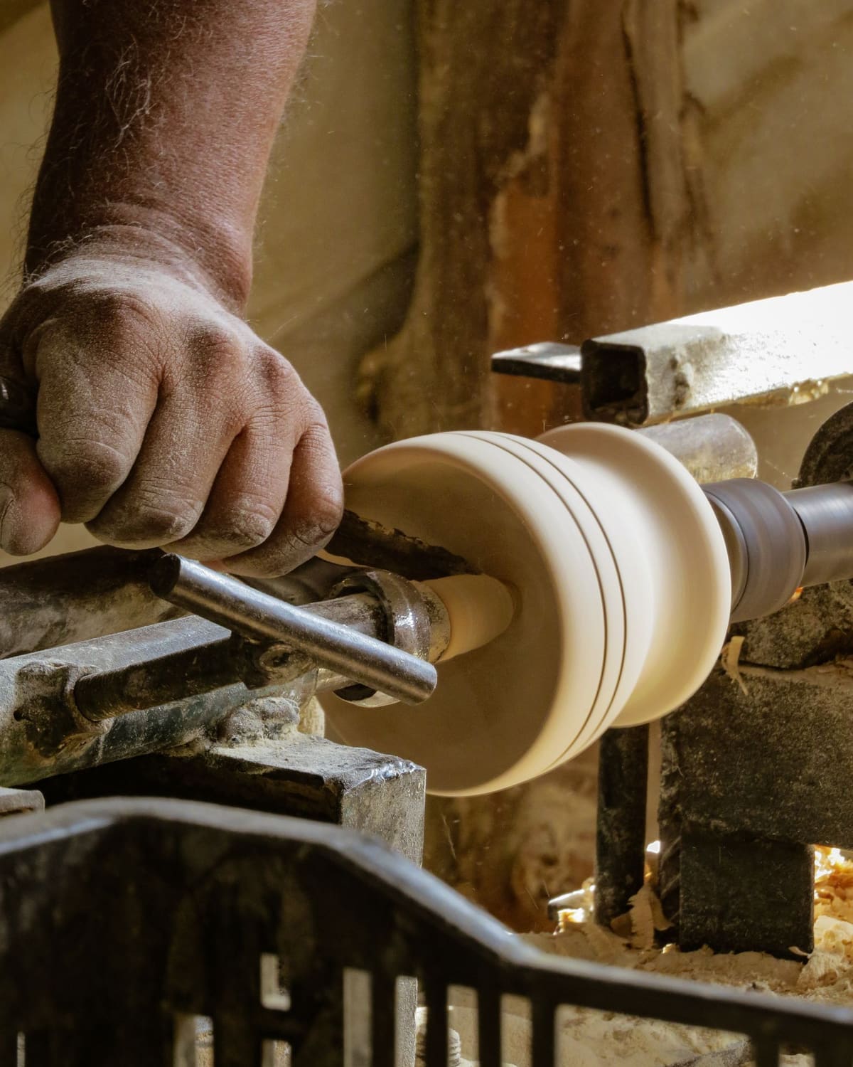 A woodturner shaping a pale bowl on a lathe, shavings flying